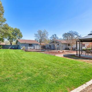 A spacious backyard with a well-maintained lawn, surrounded by trees and a fence, featuring a patio area with outdoor furniture under a clear blue sky.