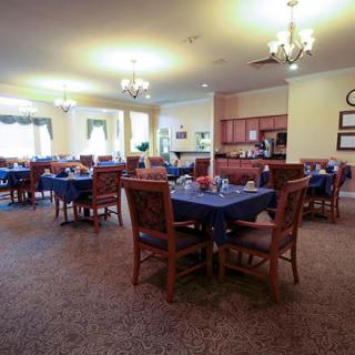 A spacious dining area with multiple tables and chairs, chandeliers, and a small kitchen in the background.