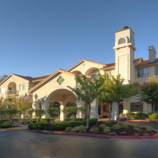 A beautiful residential building with Mediterranean-style architecture surrounded by landscaped greenery under a clear blue sky.