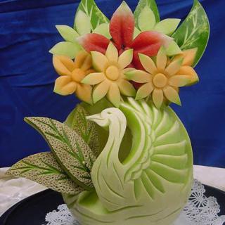 A beautifully carved fruit sculpture featuring a swan, flowers, and leaves.