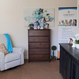 A cozy office space with a chair, dresser, and desk featuring decorative items and artwork.