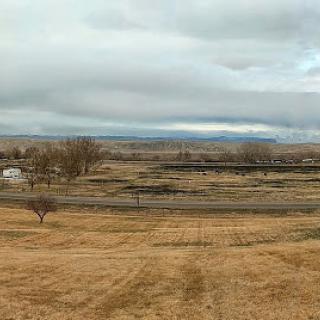 A serene rural landscape under a cloudy sky, featuring rolling fields and distant hills.