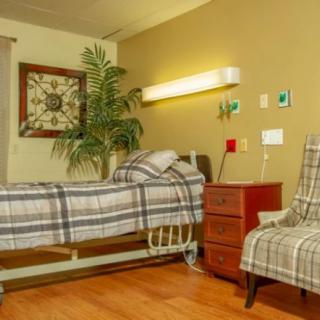 A cozy hospital room with a bed, chair, and warm decor.