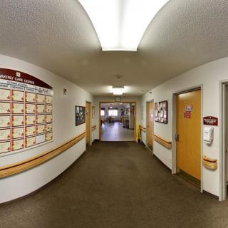 A well-lit hallway in an institutional building, featuring several doors and a notice board on the wall.