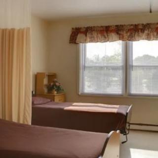 A hospital room with two beds, separated by a curtain, is illuminated by daylight coming through the window.