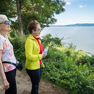 Two women enjoy a scenic view by the river, surrounded by lush greenery.