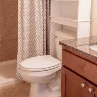 A bathroom with a toilet, sink with granite countertop, and a shower with a patterned curtain.