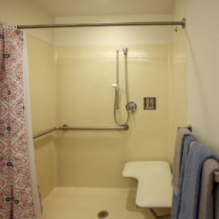 An accessible shower featuring grab bars, a shower seat, and towels neatly hanging.
