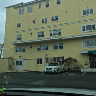 A multi-story yellow residential building with several windows and a parked car in the foreground.
