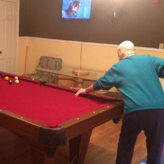 An elderly person playing billiards on a red pool table in a game room.