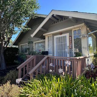 A charming house with a porch surrounded by a garden and trees on a sunny day.