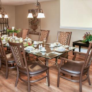 A beautifully arranged dining room with a glass table set for a meal, surrounded by elegant chairs and illuminated by a chandelier.