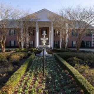 A grand mansion with a prominent fountain and landscaped garden in the foreground.
