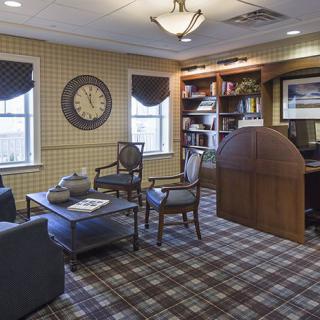 A comfortable office space with a desk, chairs, bookshelf, and large clock on the wall.