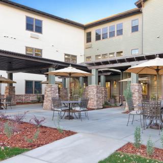A modern outdoor patio area with tables and umbrellas in front of a multi-story building.