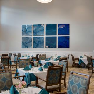 A well-lit restaurant interior with neatly arranged tables and blue-themed artwork on the wall.