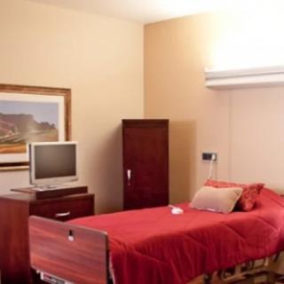 A simple hospital room with a bed, television, and wooden furniture.