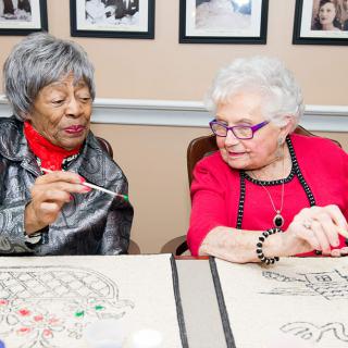 Two elderly women enjoying a crafting activity together.