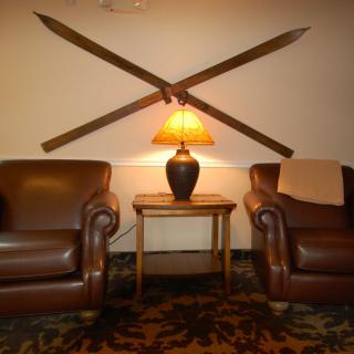 A cozy lounge area with two leather chairs, a central table with a lamp, and vintage skis as wall decor.