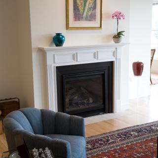 A cozy living room featuring a fireplace with decorative accents, an armchair, and artwork.