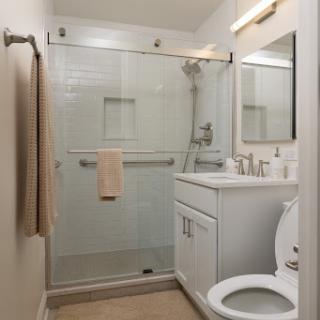 A modern bathroom featuring a glass shower, white cabinetry, and minimalist decor.