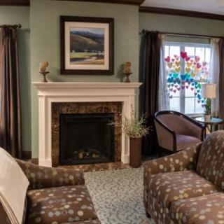 A cozy living room with a fireplace, armchairs, and a colorful stained glass window.