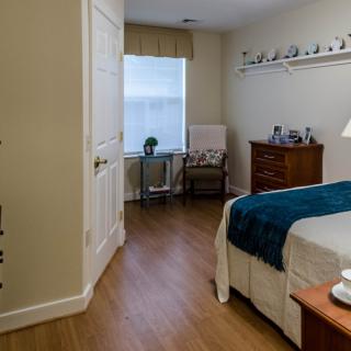 A cozy bedroom featuring a bed with blue accents, wooden flooring, a dresser, and a window with natural light.