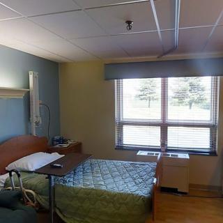 A clean and well-lit hospital room with a single bed and large windows.