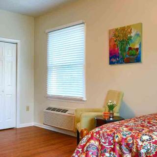 A cozy bedroom with a colorful bedspread, an armchair by the window, and artwork on the wall.