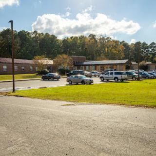 A view of a building surrounded by a parking lot, with vehicles parked and green grass in the foreground.