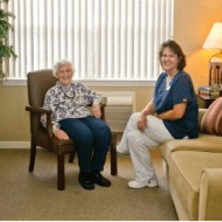 An elderly woman sitting with a caretaker in a cozy living room.