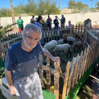 A man stands next to a fenced area containing sheep at an outdoor event.
