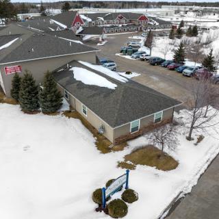 An aerial view of a building surrounded by snow, with a parking lot and trees nearby.