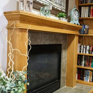 A cozy living room corner featuring a wooden fireplace mantel adorned with decorative items and surrounded by bookshelves.