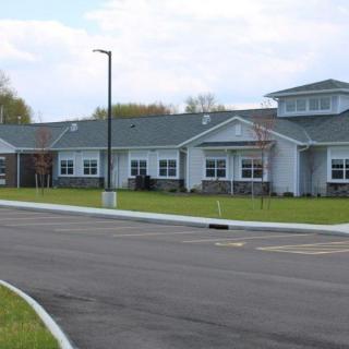 A single-story building with a sloped roof and a neatly maintained lawn in front, adjacent to a paved road.