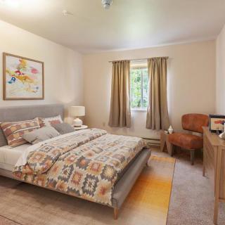 A cozy bedroom with a patterned bedspread, artwork on the wall, and warm lighting.