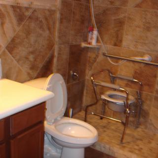 A bathroom featuring a toilet, a shower chair, and tiled walls.