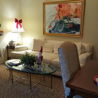 A cozy living room with holiday decorations, featuring a sofa, glass coffee table, and vibrant artwork on the wall.