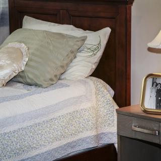 A cozy bedroom corner with a neatly made bed, pillows, and a nightstand featuring a lamp and photo frame.