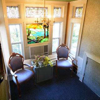 A cozy interior space featuring two chairs, a floral arrangement, and a colorful stained glass window.