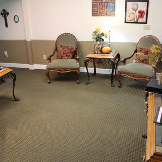 A cozy living room with chairs and a table set on a carpeted floor, adorned with artwork and decorations.