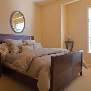 A cozy bedroom with a neatly made bed, a circular mirror on the wall, and soft lighting.