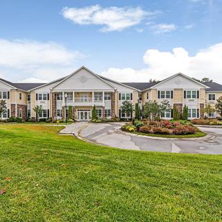 A large residential building with manicured lawns and a circular driveway under a partly cloudy sky.