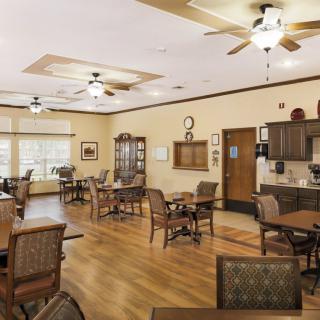 A well-lit dining area with wooden flooring, tables, chairs, and ceiling fans.