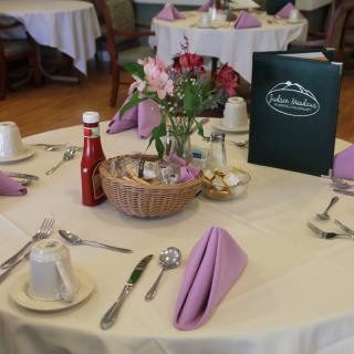 A neatly set dining table with purple napkins, a menu, and floral centerpiece.