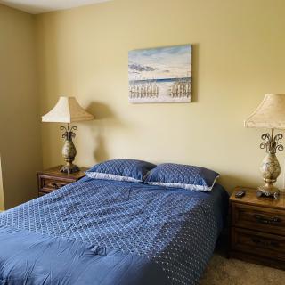 A bedroom with a neatly made bed featuring blue bedding, flanked by two lamps on nightstands, and a piece of artwork above the headboard.
