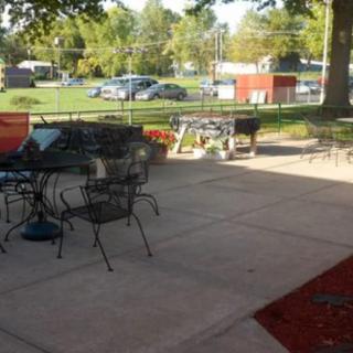 A sunny outdoor patio area with chairs, tables, and a grill overlooking a grassy yard.
