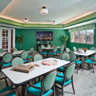 A vibrant and inviting fitness center room featuring modern tables and chairs, surrounded by green walls and decorative plants.