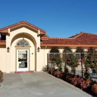 A sunny view of a one-story house with a red-tiled roof and gated entrance.