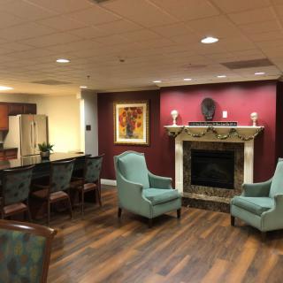 A cozy living room with armchairs around a fireplace, featuring warm decor and wood flooring.